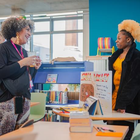 Two people speak excitedly over a stand in a library space