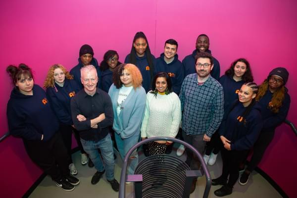 A group of people - Agents and panellists - stand in Contact on the stairs against a pink wall