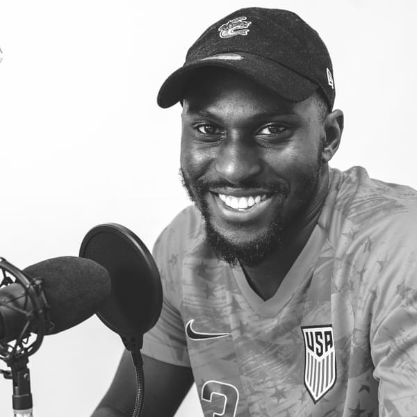 Black and white portrait of Paul Olubayo. He is wearing a cap and smiling with a recording microphone next to him.