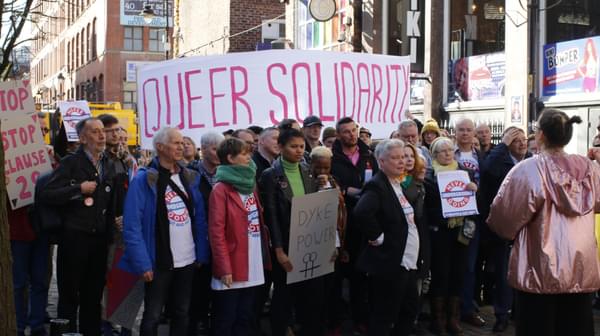 A group of people protest on Canal St in Manchester holding a large banner