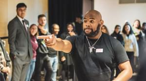 A man stands in a room surrounded by young Agents and excitedly pointing