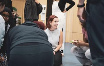 A young person with red hair kneels on the floor, laughing