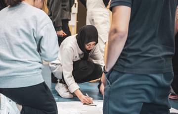 A young person draws on a sheet of paper on the floor