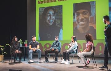 A group of young people sit on a panel on a large stage