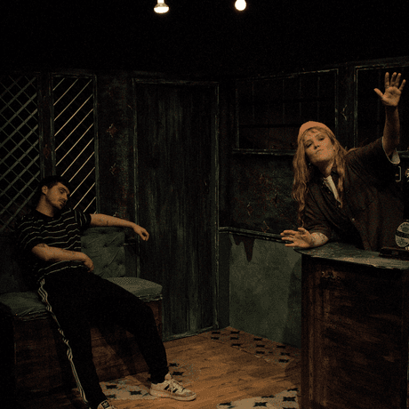 Two people perform in a studio space, gesturing wildly