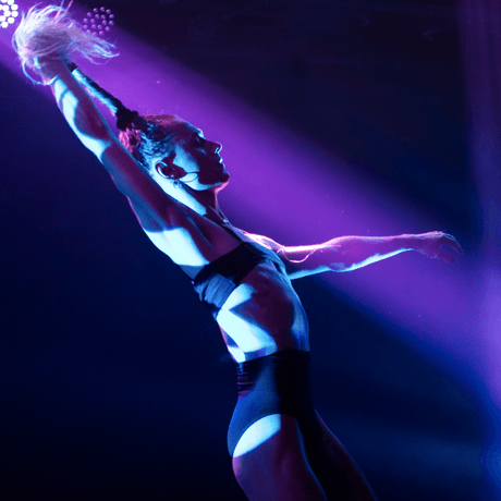 A performer is standing underneath a purple and blue spotlight.