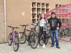 Two people standing next to a few bikes in front of the bike shed. They are smiling.