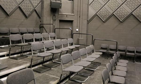 Side view of the Space 2 chairs. Five rows of tiered black chairs placed on black steps with a metal barrier on the edge.