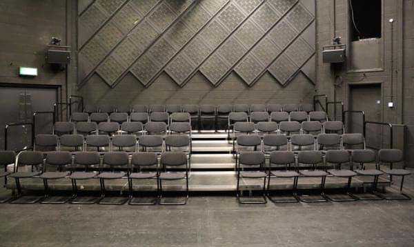Space 2 seating. Four rows of chairs with an aisle in the middle. The fifth row is at the back of the space against the wall.