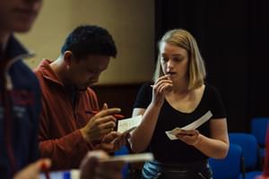 Two people chat in a room, holding notebooks