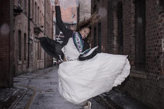 A young woman leaps in the street wearing suffragette era clothing