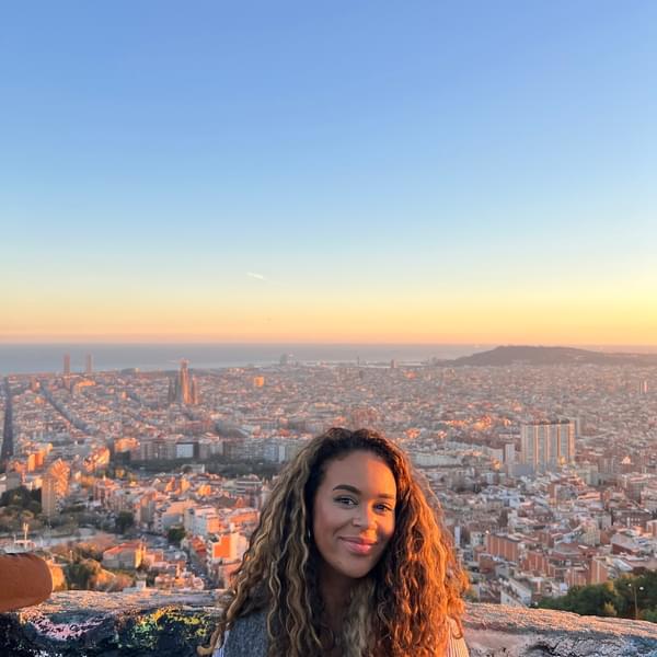 A picture of Suzanna standing on a balcony above a city, with a orange and blue sky