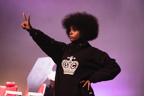 A young person on stage with afro hair holds up a peace sign