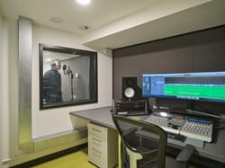 recording studio for music with person standing in the booth and the long screen computer in the room in front of it