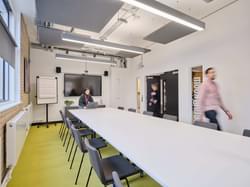 meeting room with long conference table in the middle and large screen at the end of the room. people walking into the room as if they are about to start a meeting