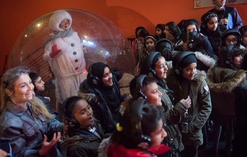 A member of Contact Young Company, dressed as a snowman, performs for a group of smiling, excited children during a production of The Siege of Christmas