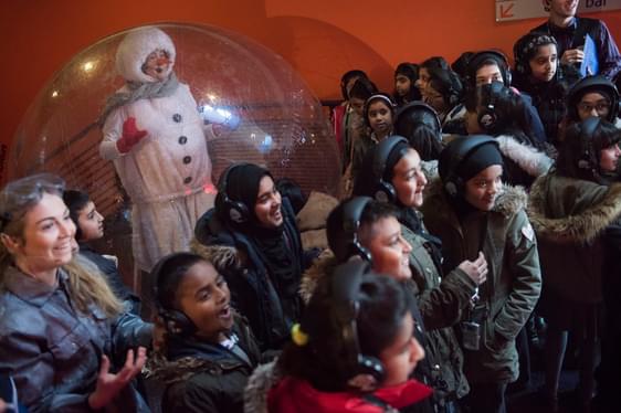 A member of Contact Young Company, dressed as a snowman, performs for a group of smiling, excited children during a production of The Siege of Christmas
