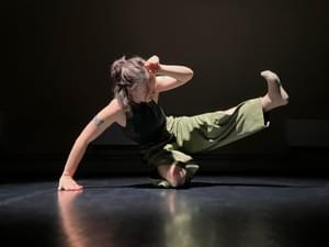 A person on a stage dancing, they are on one knee with the other leg kicked in the air.