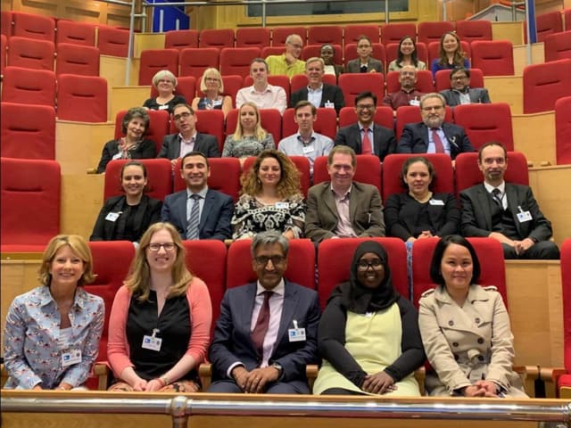 28 professional people sitting in multiple rows in a theater.