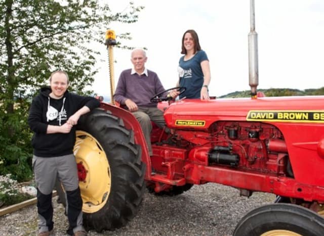 Three people posing with a big red tractor.