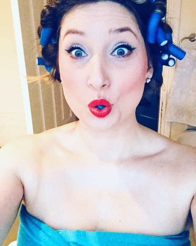 A surprised woman with curlers in her hair in the bathroom.