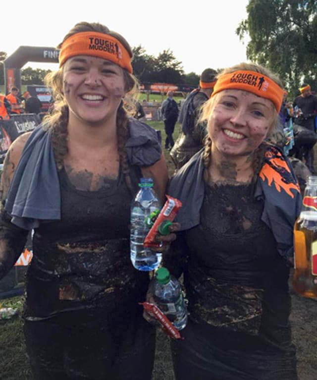 Two smiling women covered in mud after completing a Tough Mudder.