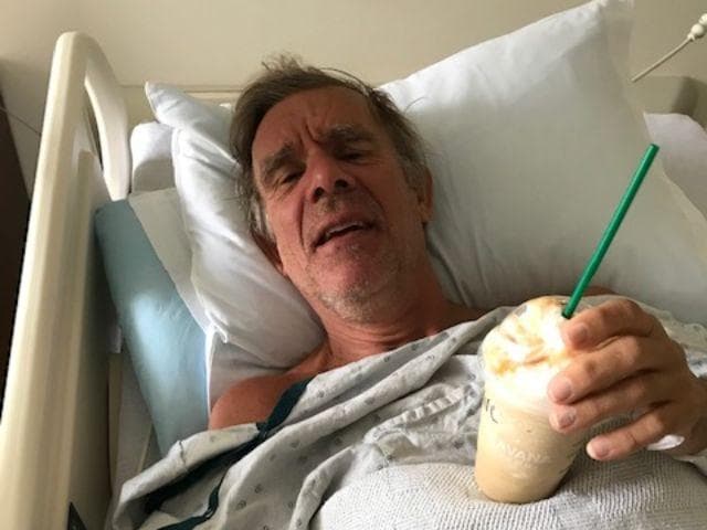 A man laying in a hospital bed with a Starbucks frozen drink.