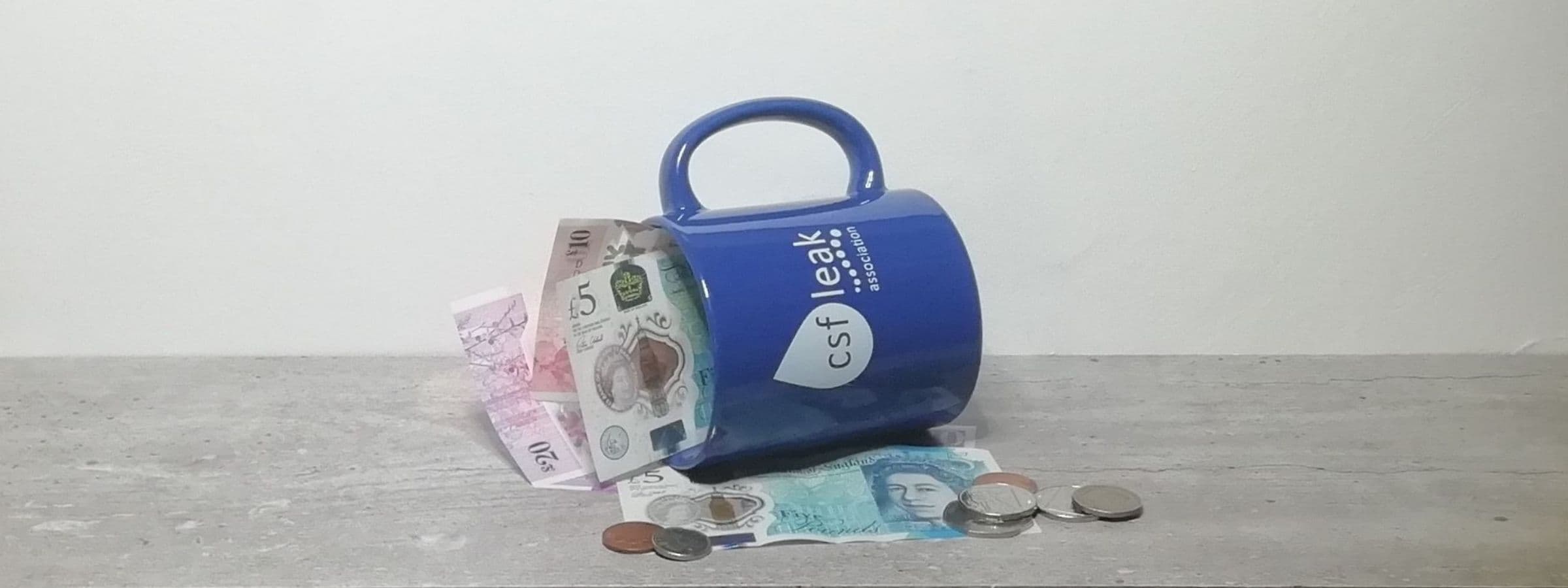 Blue mug saying CSF Leak Association with British currency.