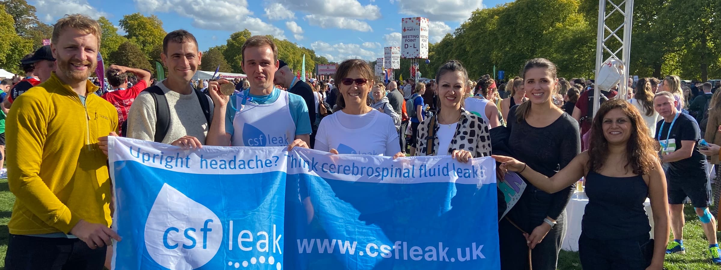 A group of runners and supporters smiling holding a large flag that says CSF Leak Association.