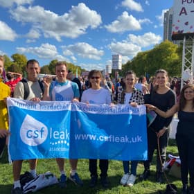 A group of runners and supporters smiling holding a large flag that says CSF Leak Association.
