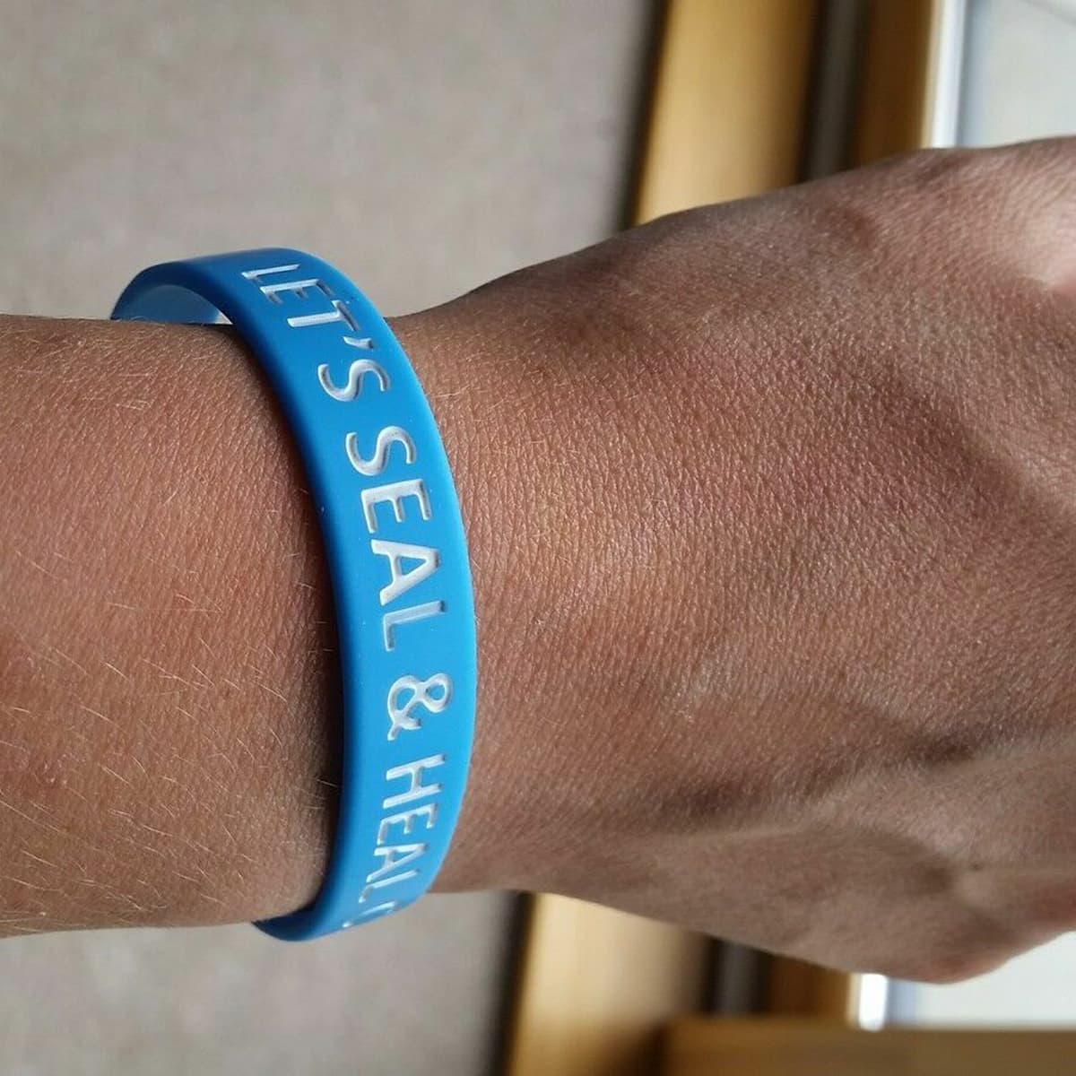 A wrist with a blue wrist band that says "let's seal and heal csf leaks".