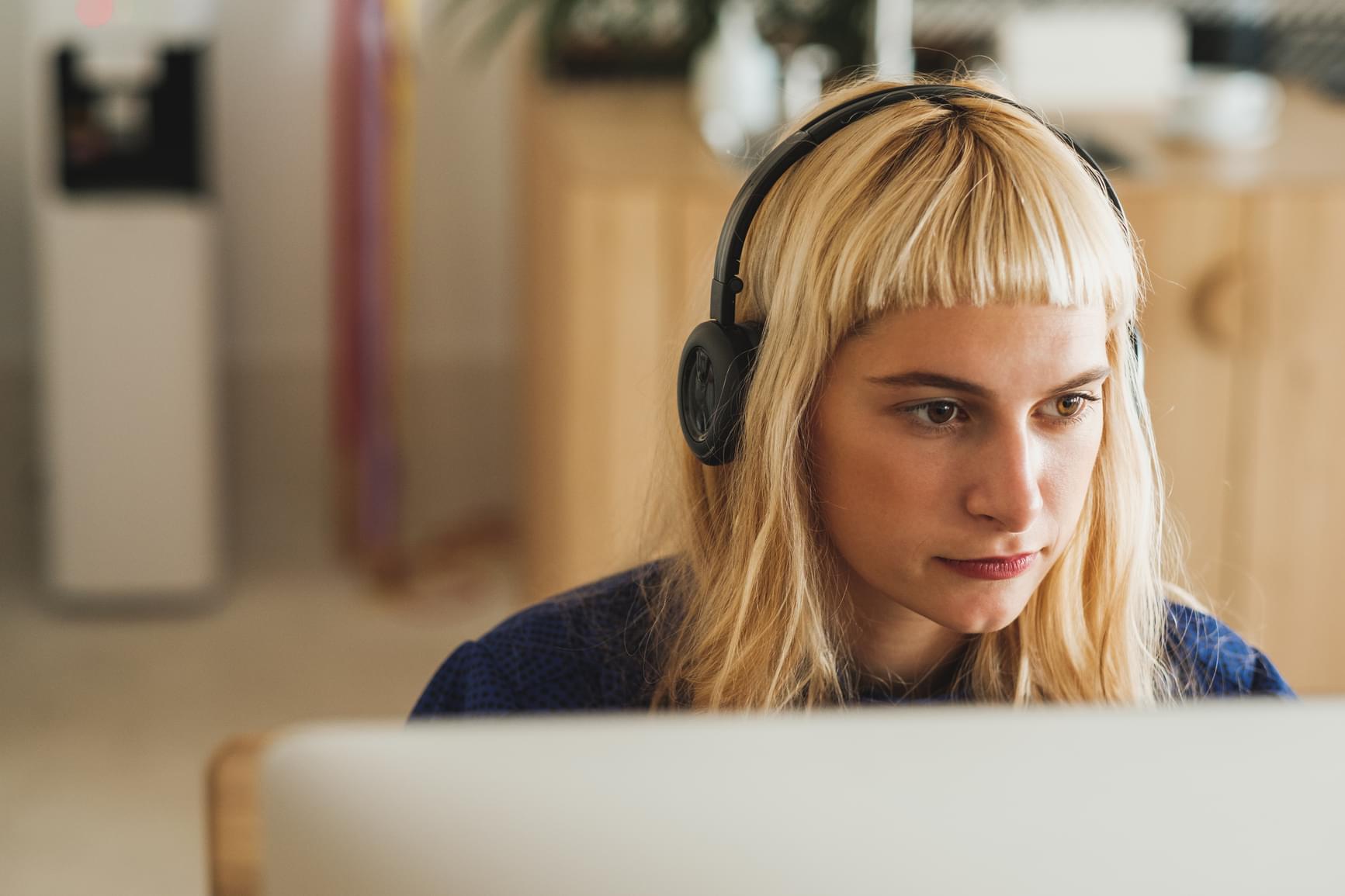 Quiply Blonde Junge Frau mit Kopfhören sitzt vor iMac