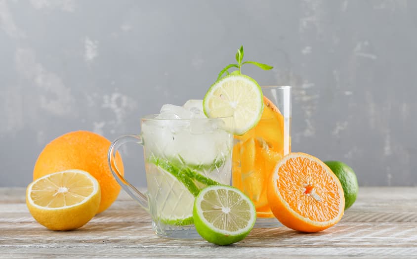 Detox water with limes lemons oranges mint cup glass wooden table side view