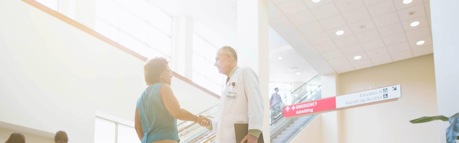 A Doctor shaking hands with a woman in the lobby of a hospital.
