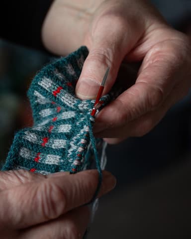 Maureen White, Hand Knitting Artisan X  Johnstons of Elgin hand knitting a green and red fairisle. Proceeds go to the Longhope Lifeboat service.