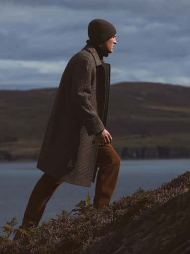 Johnstons of Elgin Limited Edition Balmacaan Coat shot on a Scottish moorland and worn with brown cords and a green beanie