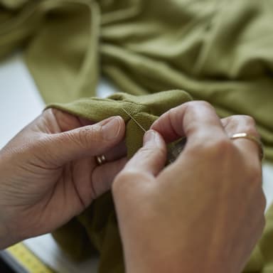 Johnstons of Elgin craftsperson hand stitching the label in a green sweater