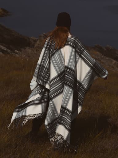 Johnstons of Elgin Limited Edition Black and White Stewart Tartan Cape shot on a Scottish moorland and worn with a black cashmere beanie