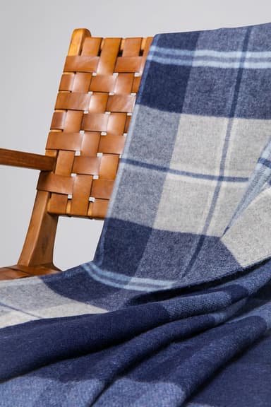 Johnstons of Elgin Reversible Lambswool Throw in Blue Check on a brown chair