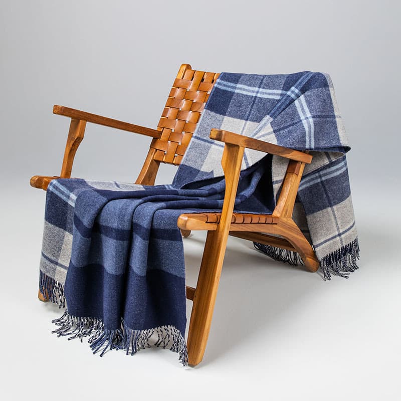 Johnstons of Elgin Lambswool Blanket in a reversible blue check on a wooden lattice chair