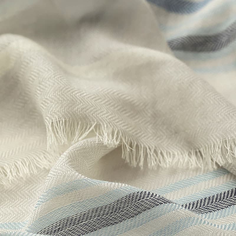 Close up of a Johnstons of Elgin Merino Scarf with blue and white stripes and feathered fringing