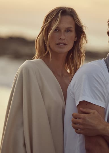 Johnstons of Elgin Natural Cashmere Stole draped over a models shoulder on a beach at sunset