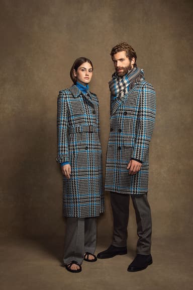 Johnstons of Elgin men's and women's blue & black tweed coats paired with matching trousers on a beige background