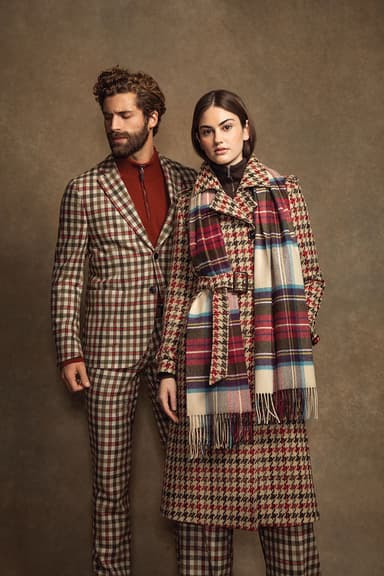 Johnstons of Elgin men's and women's red and camel tweed coats paired with matching trousers on a beige background