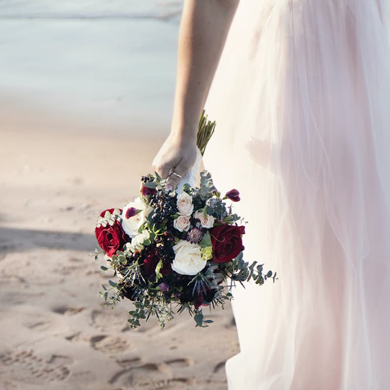 Bride on beach with red and white floral bouquet