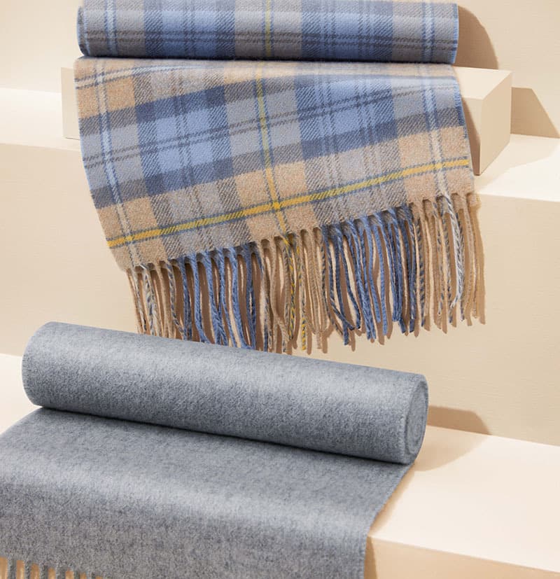 Johnstons of Elgin Woven Cashmere Scarves in Campbell Tartan and Mid Grey draped over beige steps