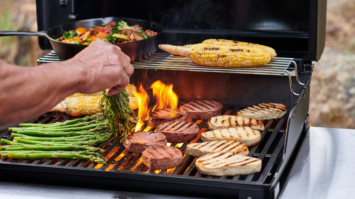A close up shot of a grill top with vegetables and meati products being grilled