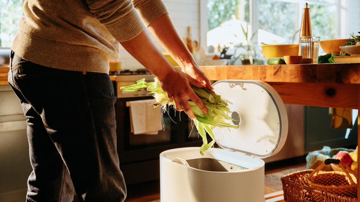 In a bright kitchen a man is throwing corn husks in a compost bin