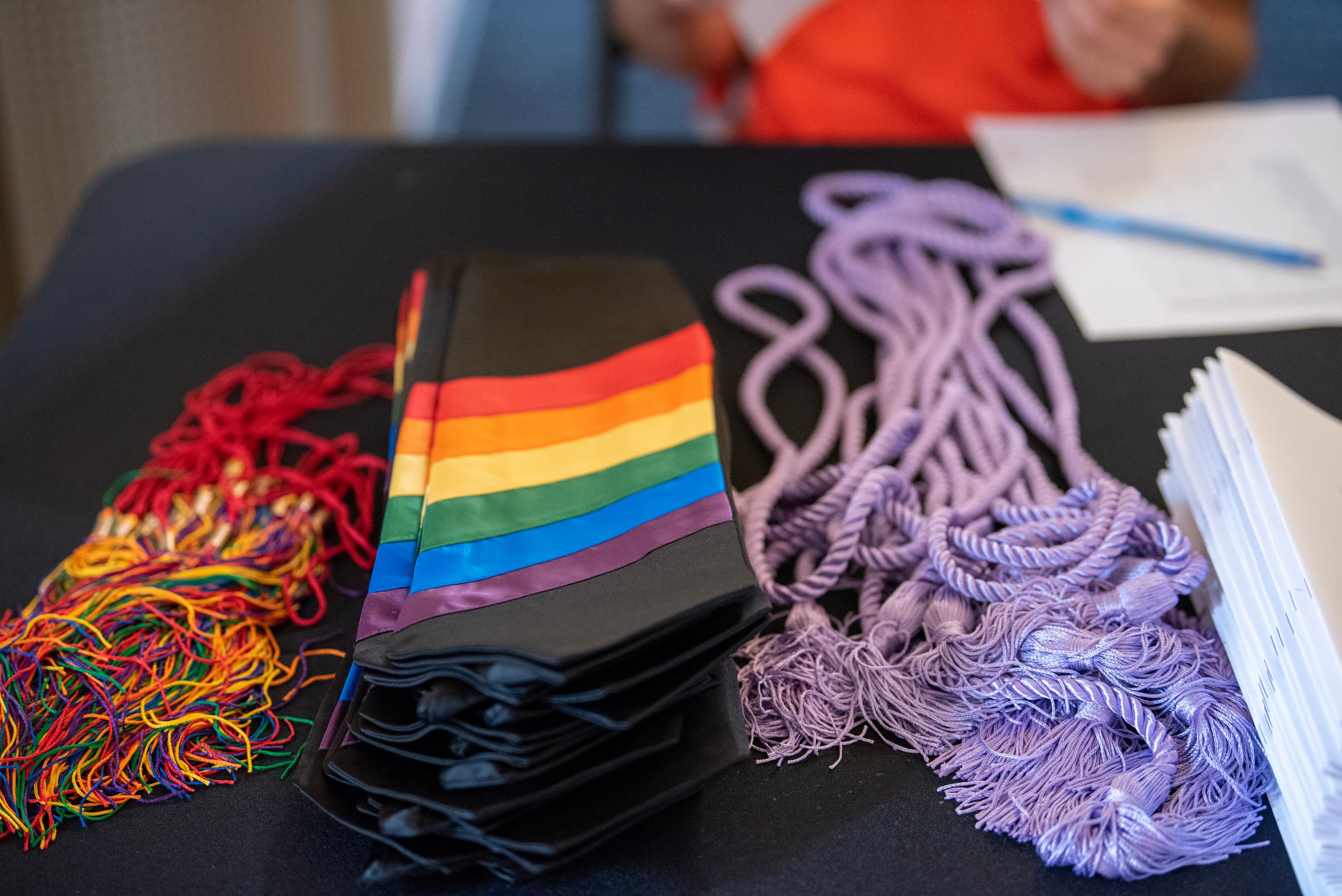 Photo of rainbow tassels and stoles, plus lavender cords on a black table.