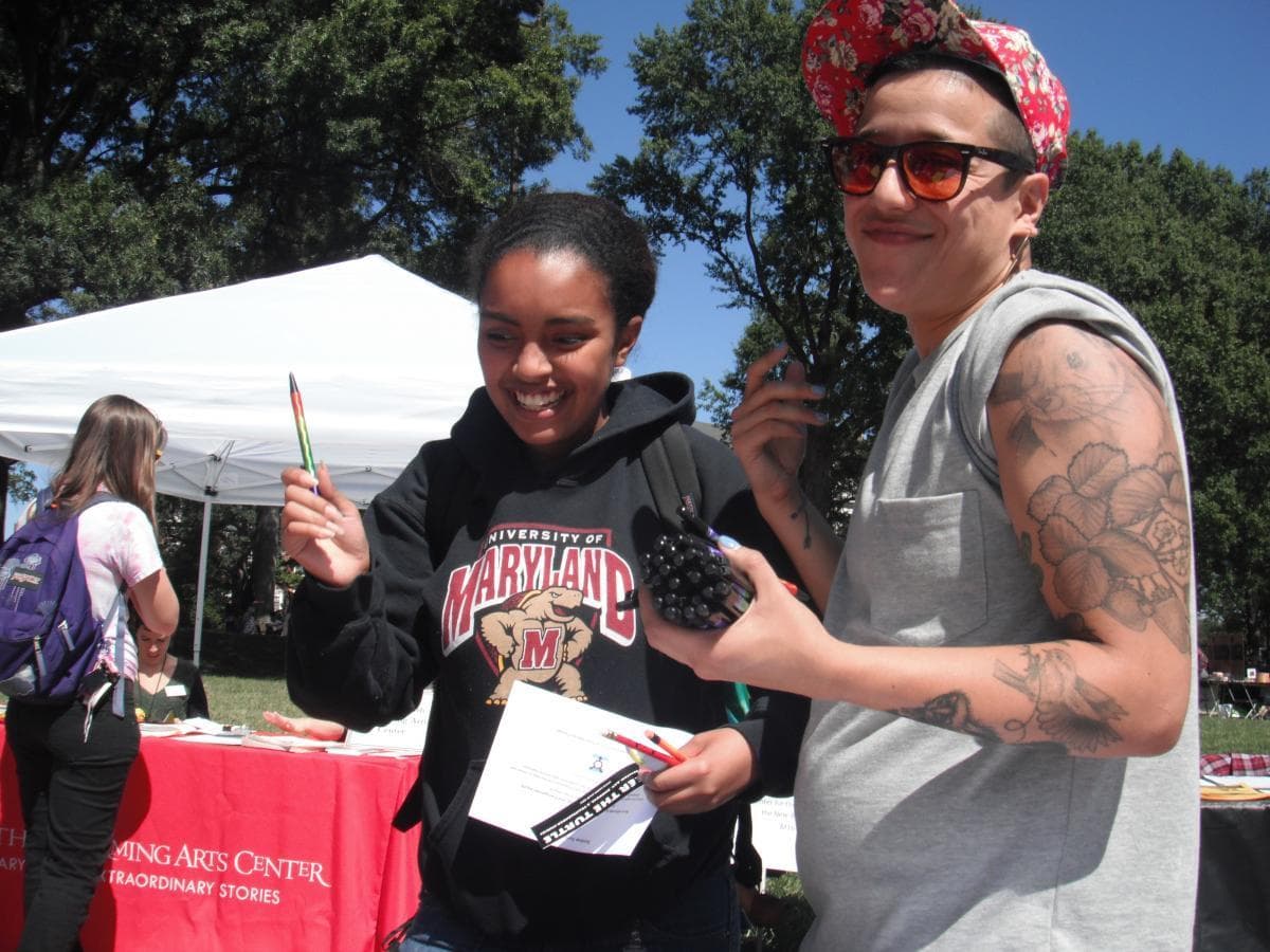 Two members of Speakers Bureau handing out pens at an outside event.